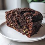 Close-up of a rich, dark slice of Top Rated Moist Chocolate Zucchini Cake showing green shreds of zucchini baked inside.