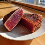 Two halves of a perfectly seared tuna steaks cast iron skillet preparation, showing a bright red, rare interior and a dark, seasoned crust.