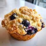 Close-up of an ultimate blueberry muffin cookie featuring a thick, crunchy streusel topping and bursting blueberries.