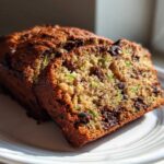 A close-up of a sliced loaf of Ultimate Moist Chocolate Chip Zucchini Bread on a white plate.
