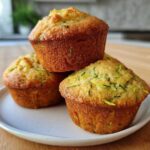 A stack of three golden-brown Ultimate Moist Zucchini Muffins with visible shreds of green zucchini.