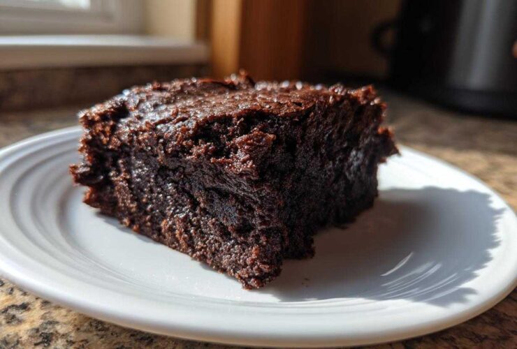 A close-up of a rich, fudgy slice of Vegan Avocado Zucchini Brownies on a white plate.