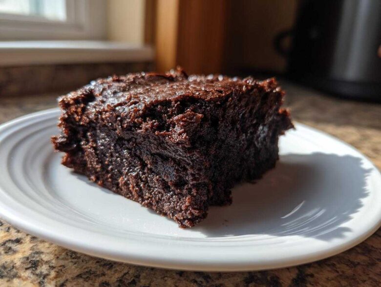 A close-up of a rich, fudgy slice of Vegan Avocado Zucchini Brownies on a white plate.