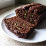 A close-up of a dark, moist slice of Vegan Chocolate Zucchini Bread showing shreds of green zucchini throughout the crumb.