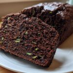 Close-up of a moist, dark chocolate Vegan Chocolate Zucchini Bread loaf with two slices cut, showing flecks of green zucchini.