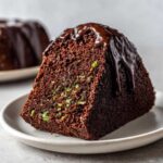 Close-up of a slice of rich, dark Vegan Chocolate Zucchini Cake topped with dripping chocolate ganache.