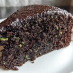 Close-up of a moist slice of Trending Vegan Chocolate Zucchini Cake showing dark chocolate crumb and green zucchini shreds.