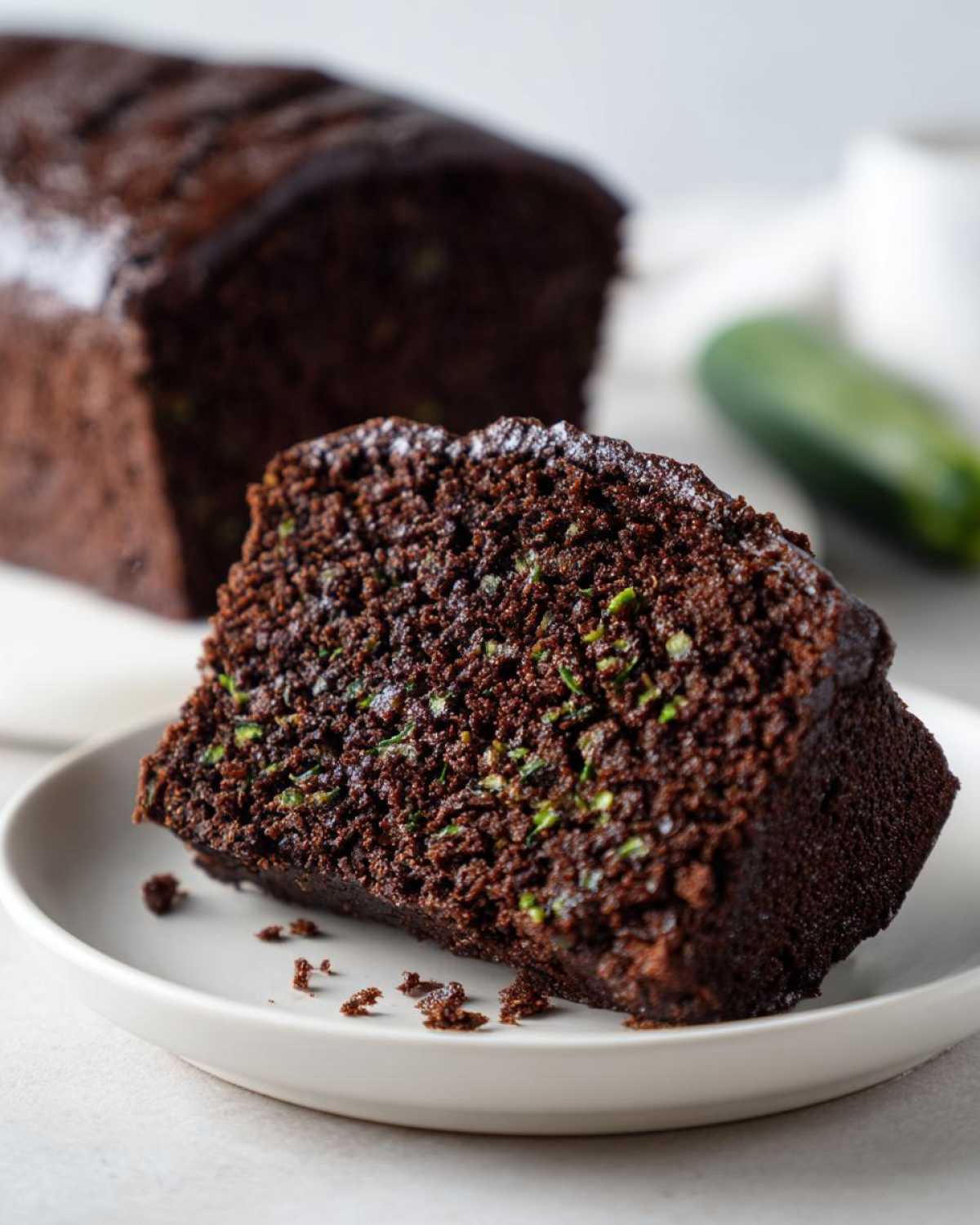 Close-up of a moist slice of rich chocolate zucchini cake showing flecks of green zucchini inside.