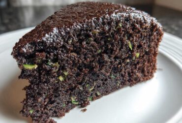 Close-up of a moist slice of Trending Vegan Chocolate Zucchini Cake showing dark chocolate crumb and green zucchini shreds.