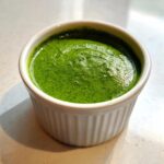Close-up of bright green, freshly blended cilantro lime sauce served in a small, white, fluted ramekin.