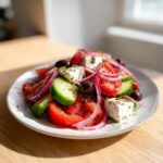 Close-up of a fresh Greek salad featuring large chunks of feta, bright red tomatoes, cucumber slices, red onion, and Kalamata olives.