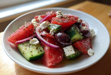 Close-up of a fresh Greek salad featuring chunks of tomato, cucumber, red onion, feta cheese, and Kalamata olives, seasoned with herbs.