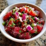 Close-up of bright red, cubed tuna in a white bowl, mixed with diced red onion and cilantro for tuna ceviche.