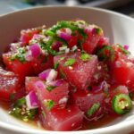 Close-up of bright red tuna ceviche cubes mixed with red onion, cilantro, and jalapeño slices.