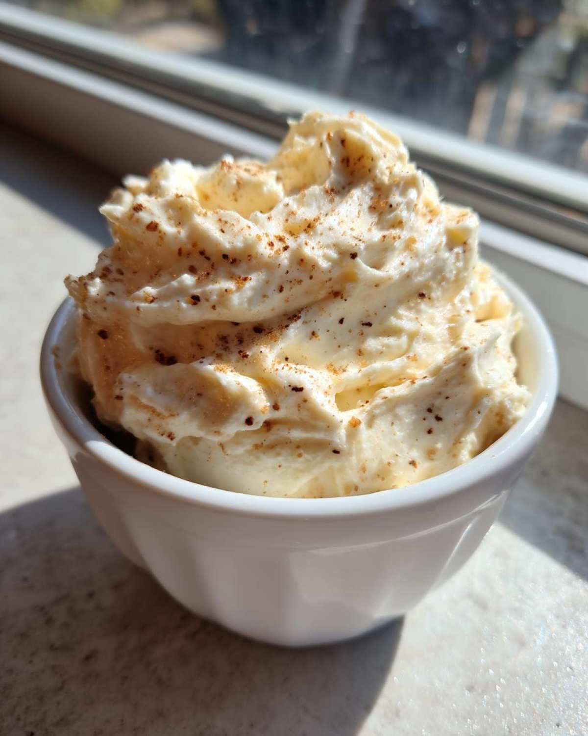 A close-up of fluffy, whipped cinnamon butter sprinkled with ground cinnamon, served in a small white ramekin.