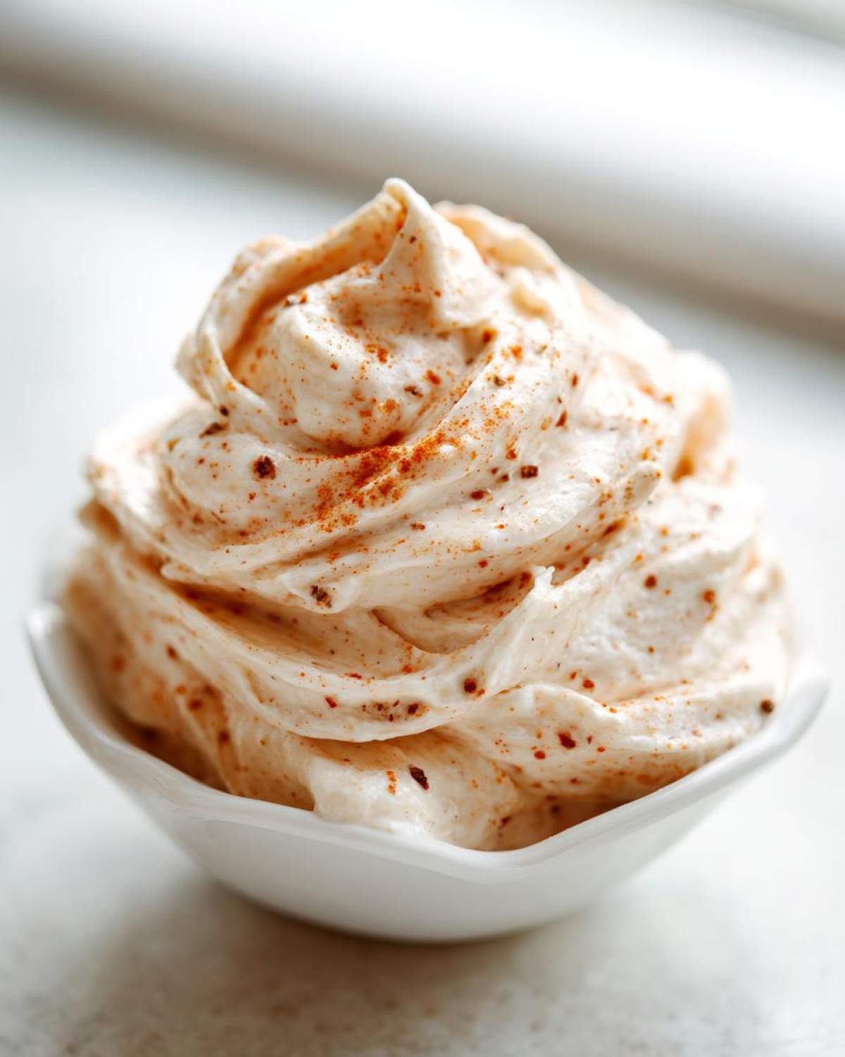 A swirl of creamy, whipped cinnamon butter sprinkled with visible cinnamon spice in a small white dish.