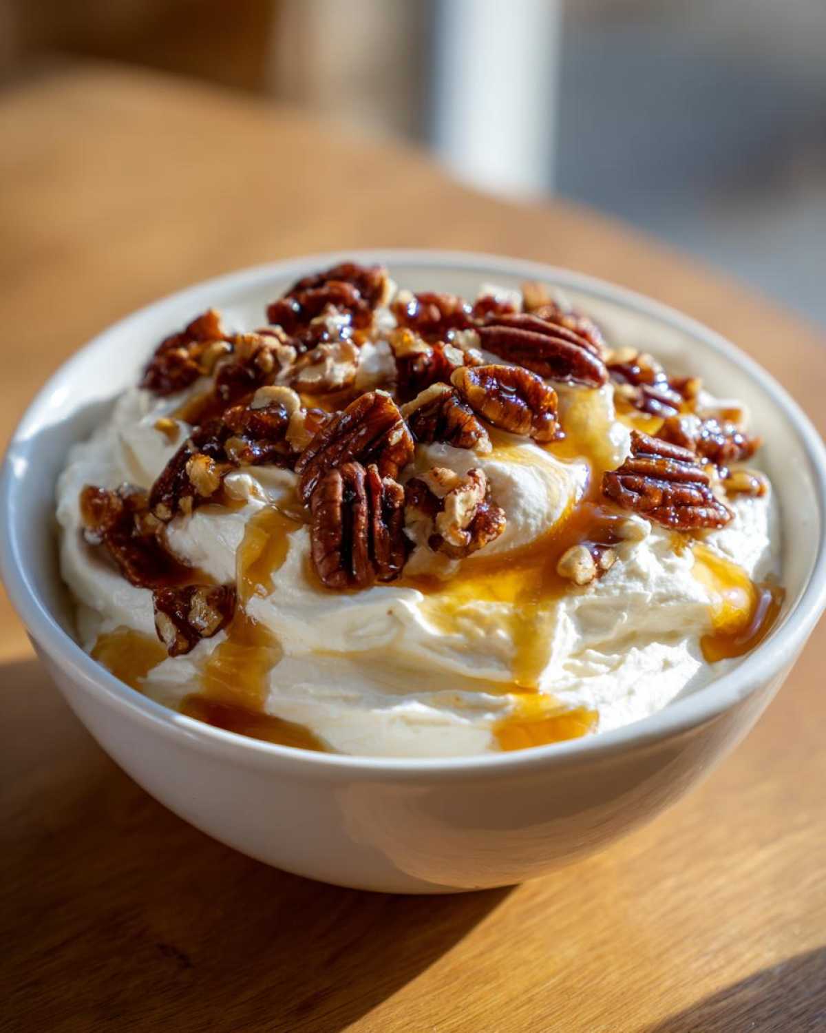 A white bowl filled with creamy whipped goat cheese topped with candied pecans and a drizzle of honey.
