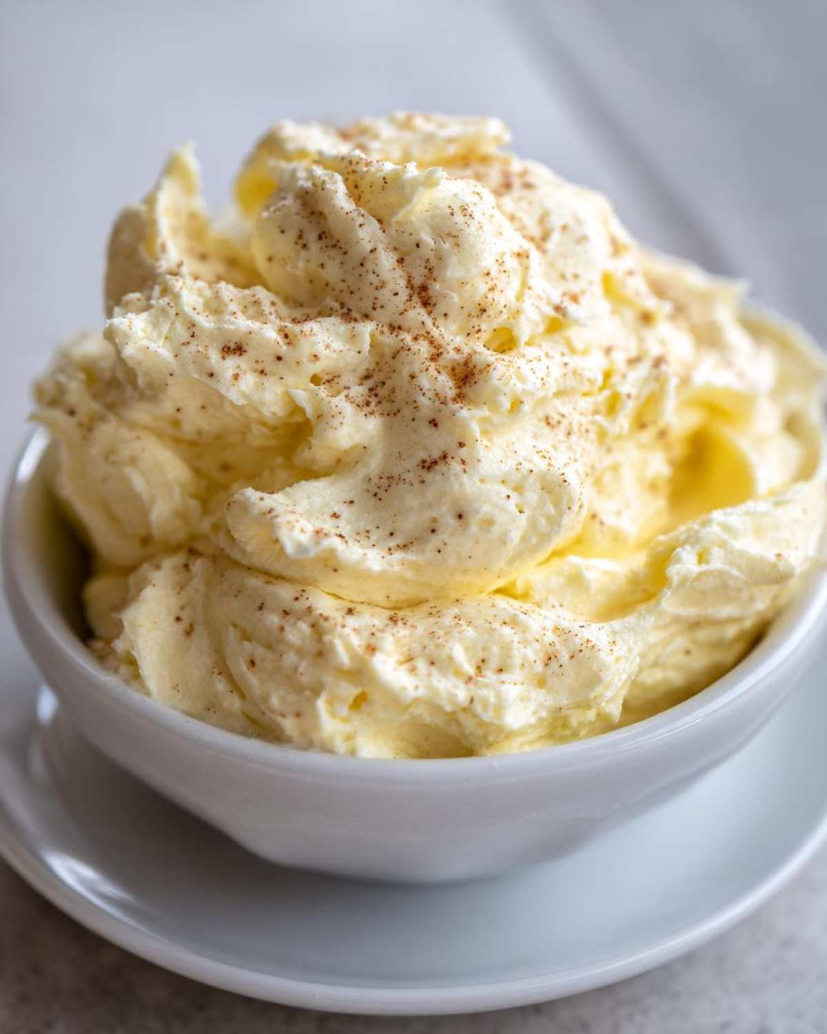 Close-up of fluffy, whipped honey butter sprinkled with cinnamon, served in a small white bowl.