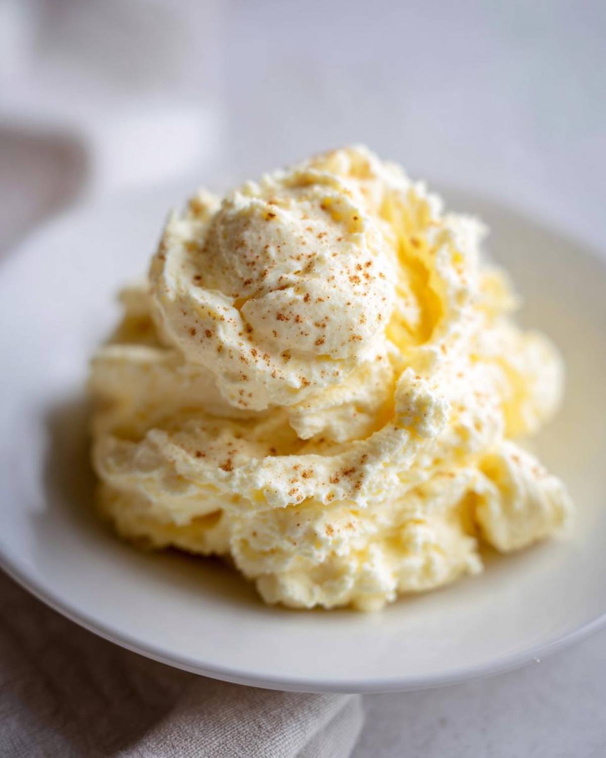 A fluffy dollop of whipped honey butter, lightly sprinkled with cinnamon, served on a white plate.