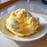 Close-up of fluffy, light yellow whipped honey butter recipe served in a white bowl, showing specks of spice.