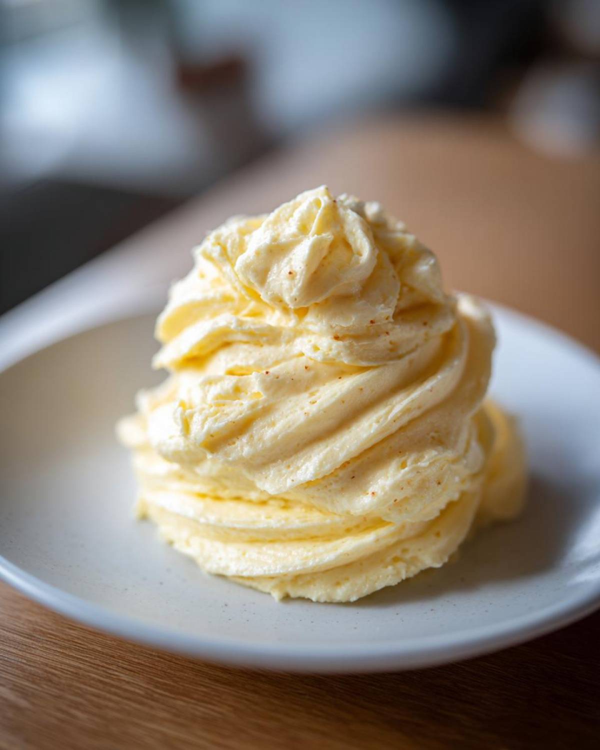 A tall swirl of light yellow, whipped honey butter recipe mixture piped onto a small, light gray plate.
