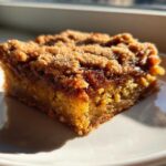 A close-up, sunlit view of a single square of Zucchini Crumble Bars with a thick, golden-brown streusel topping.