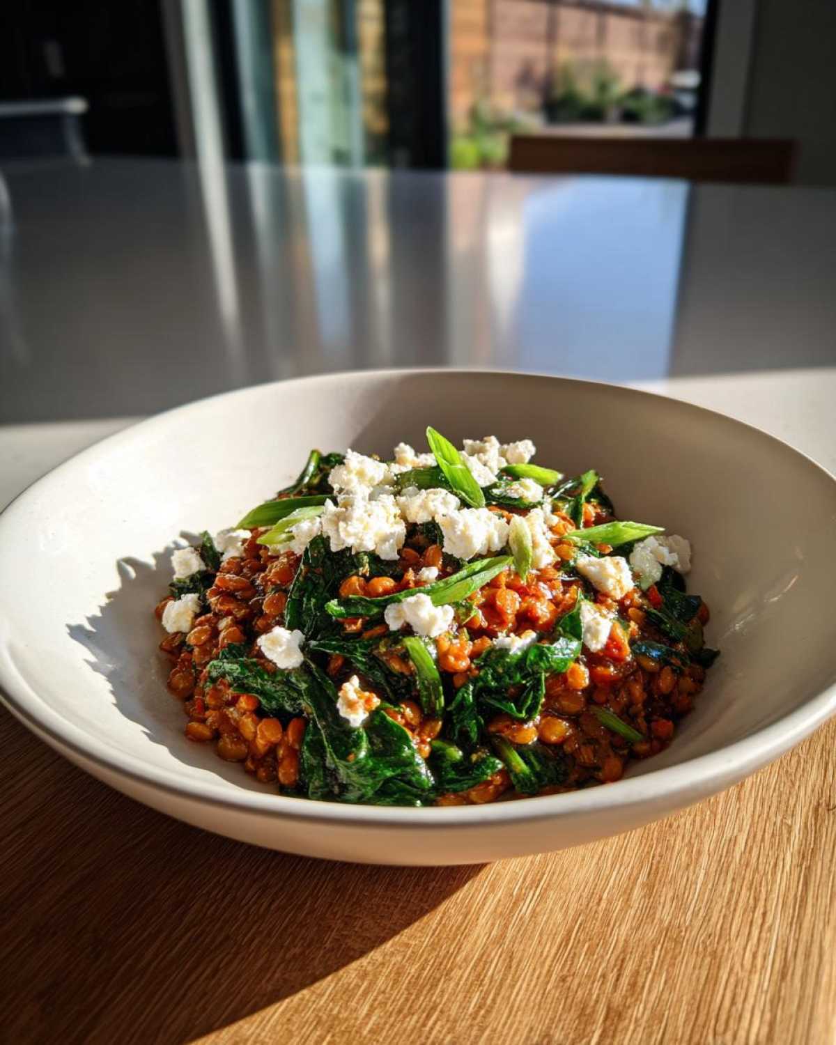 A white bowl filled with 1 Pot Feta and Lentil Spinach Dinner, topped with crumbled feta and green onions.