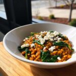 A close-up of a white bowl filled with 1 Pot Feta and Lentil Spinach Dinner, topped with crumbled feta.