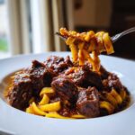 Close-up of fork lifting rich, slow-cooked beef ragu mixed with wide egg noodles, showcasing The Authentic Flavor Experience.