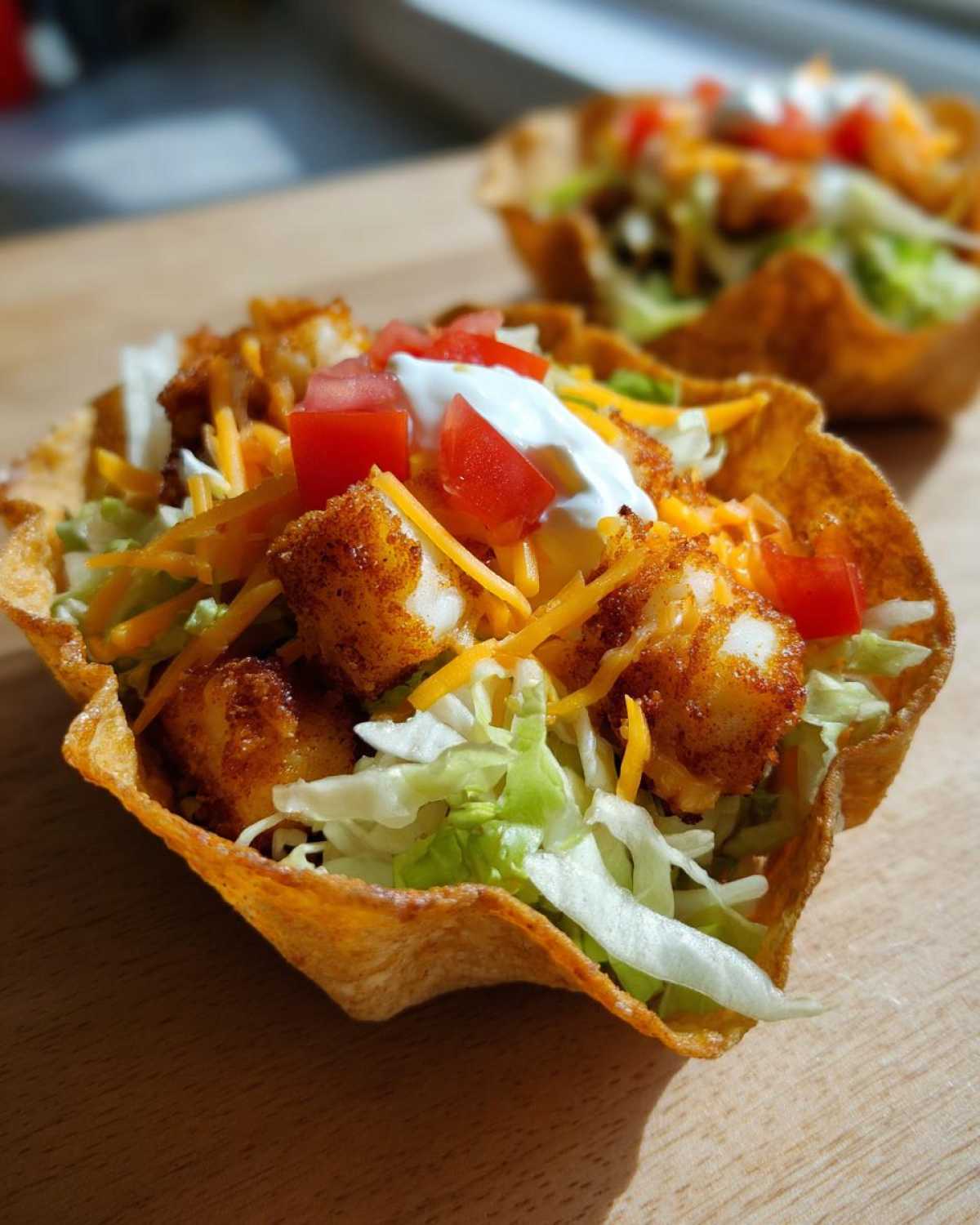Close-up of a crispy taco shell filled with air fried fish, lettuce, cheese, tomatoes, and sour cream, representing Air Fried Fish Walking Tacos.