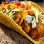 A close-up view of a crispy taco shell filled with golden Air Fried Fish Walking Tacos toppings.