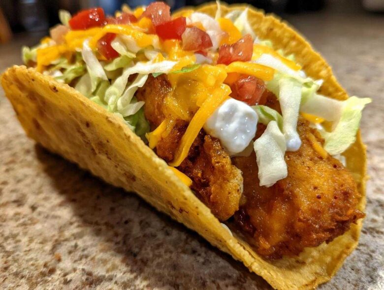 A close-up view of a crispy taco shell filled with golden Air Fried Fish Walking Tacos toppings.