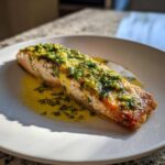 A golden-brown fillet of Air Fryer Fish topped with melted butter, garlic, and fresh dill, resting in a pool of sauce.