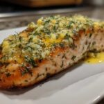 Close-up of a perfectly cooked salmon fillet prepared using the Air Fryer Fish method, topped with melted butter, garlic, and herbs.