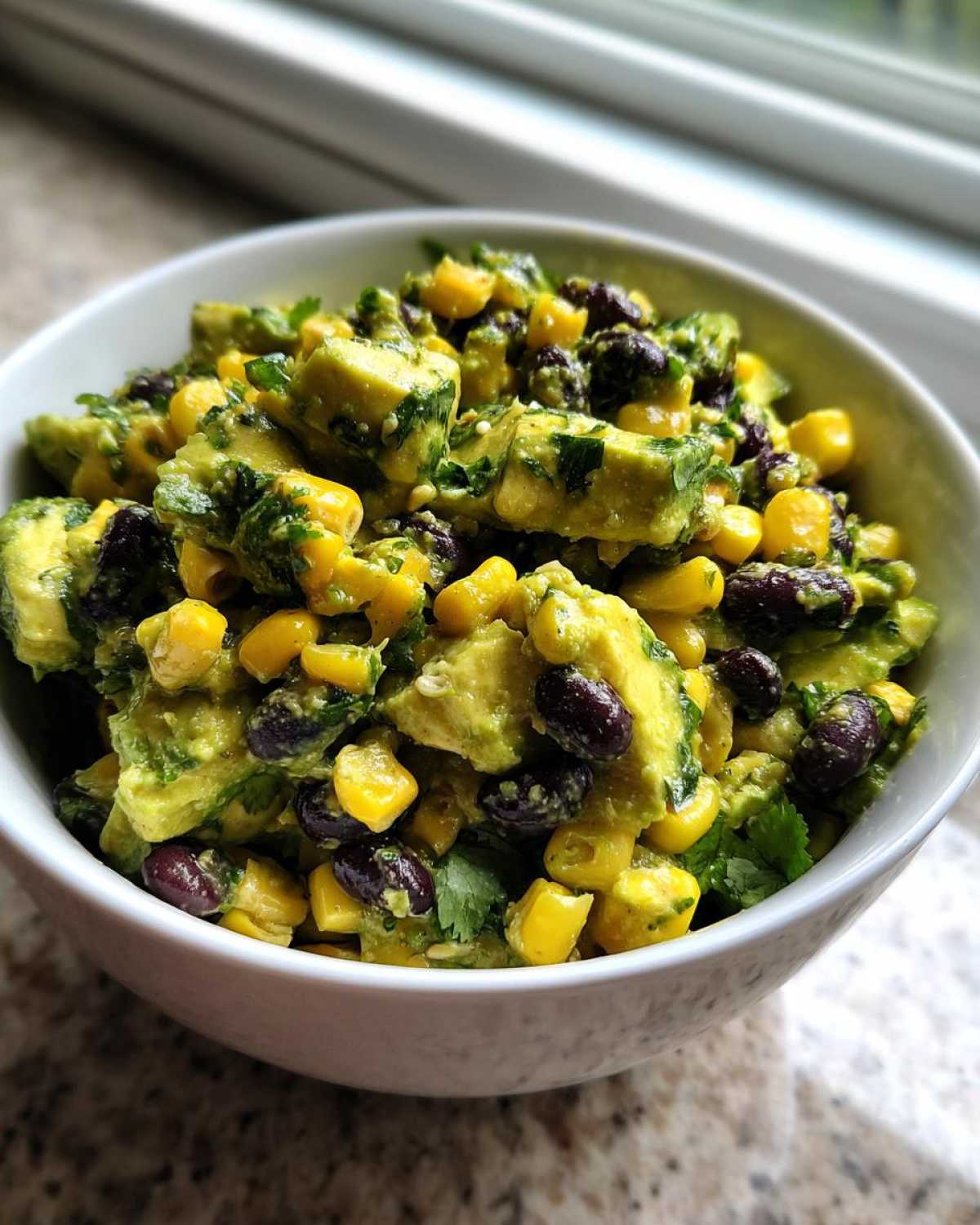 Close-up of a fresh Avocado Salad mixed with bright yellow corn kernels and dark black beans in a white bowl.