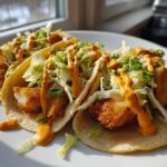 Three delicious Baja Fish Tacos filled with crispy fish, shredded cabbage, and drizzled with orange sauce.