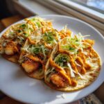 Three delicious Baja Fish Tacos filled with crispy fish, shredded cabbage, and drizzled with a spicy orange sauce.