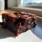 A close-up of a rich, fudgy square of Banana Bread Brownies with visible chocolate chips, sitting on a white plate.