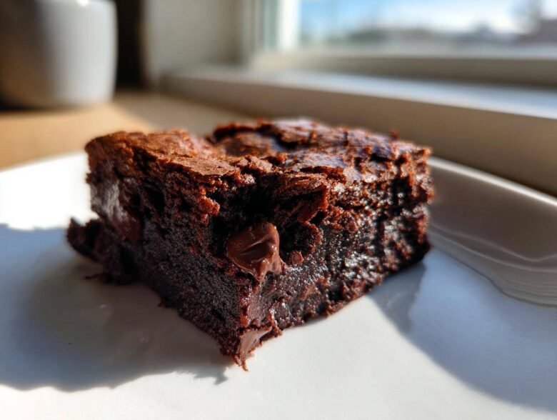 A close-up of a rich, fudgy square of Banana Bread Brownies with visible chocolate chips, sitting on a white plate.