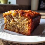 Close-up of a moist slice of Banana Bread Snack Cake Soft Moist Treat with a shiny, caramelized topping on a white plate.