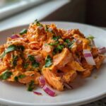 A close-up of a serving of vibrant orange Bang Bang Salmon Salad mixed with red onion and topped with fresh cilantro.