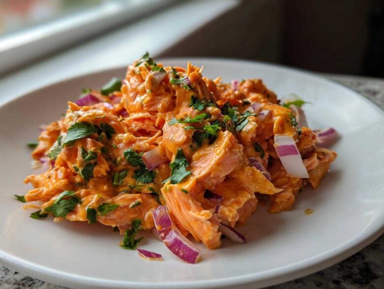 A close-up of a serving of vibrant orange Bang Bang Salmon Salad mixed with red onion and topped with fresh cilantro.