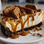 A thick slice of creamy Biscoff Cheesecake topped with caramel sauce and whole Biscoff cookies.