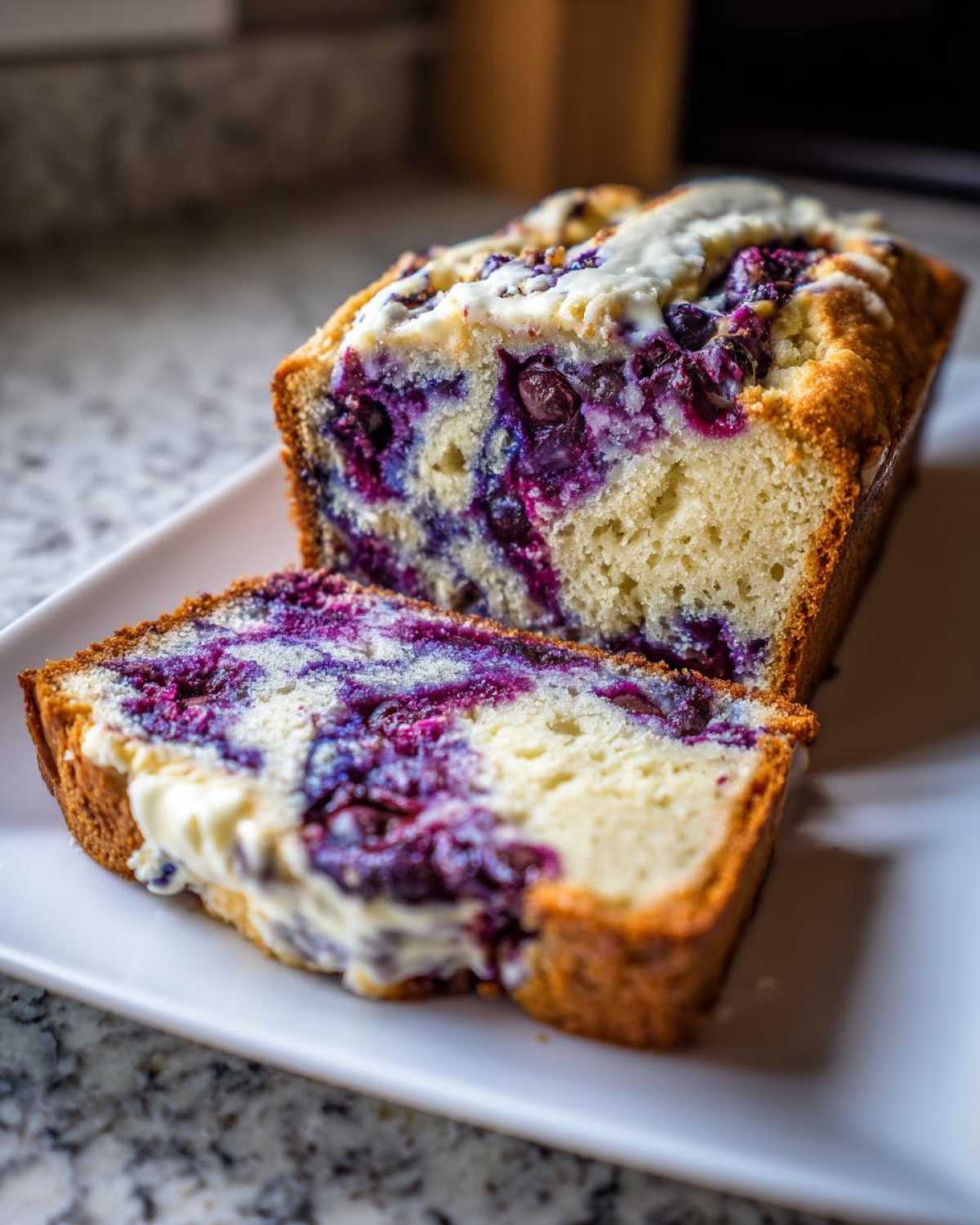 A close-up of a sliced Blueberry Cream Cheese Bread Loaf showing the rich purple blueberry swirl and cream cheese topping.