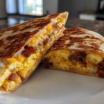A cross-section view of a golden-brown Breakfast Crunchwrap filled with scrambled eggs, cheese, bacon, and potatoes.