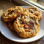 A stack of freshly baked Brown Butter Kitchen Sink Cookies loaded with chocolate chunks and pretzels on a white plate.