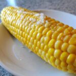 Close-up of a bright yellow ear of Buttered Corn sprinkled generously with coarse salt.
