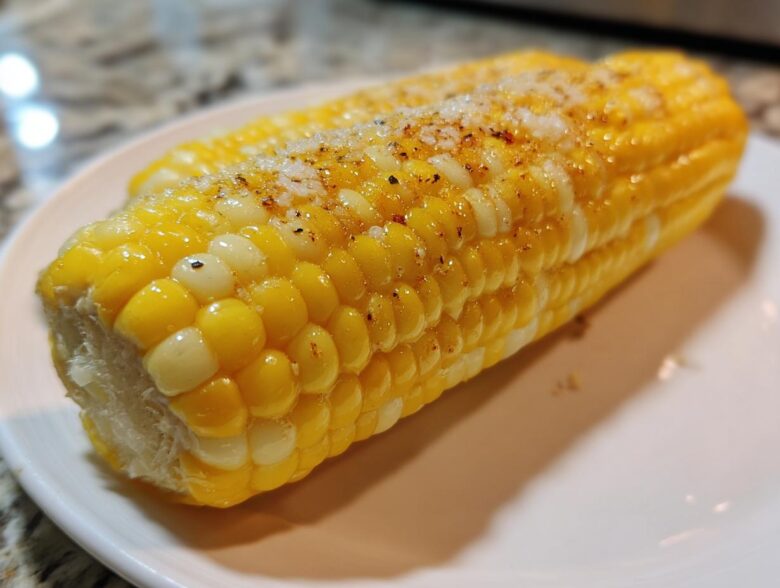 Close-up of two ears of cooked Buttered Corn on the cob glistening with butter and topped with salt and pepper.
