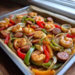 Close-up of seasoned Cajun Shrimp and Sausage Sheet Pan with colorful bell peppers and onions on a baking tray.