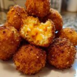 A close-up of golden-brown, crispy Cheesy Mashed Potato Balls, one of which is broken open revealing melted cheddar cheese inside.